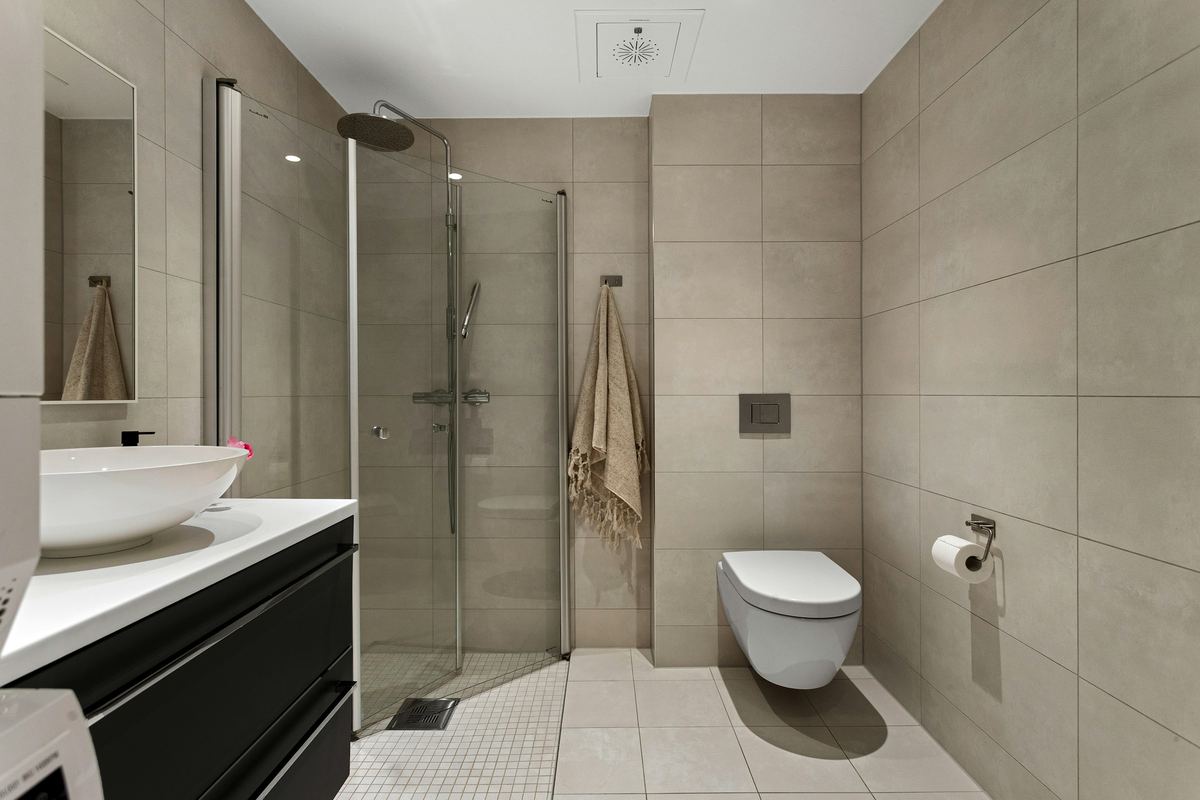 Afgewerkte badkamer met grijze tegels, inloopdouche, hangtoilet en wastafelmeubel