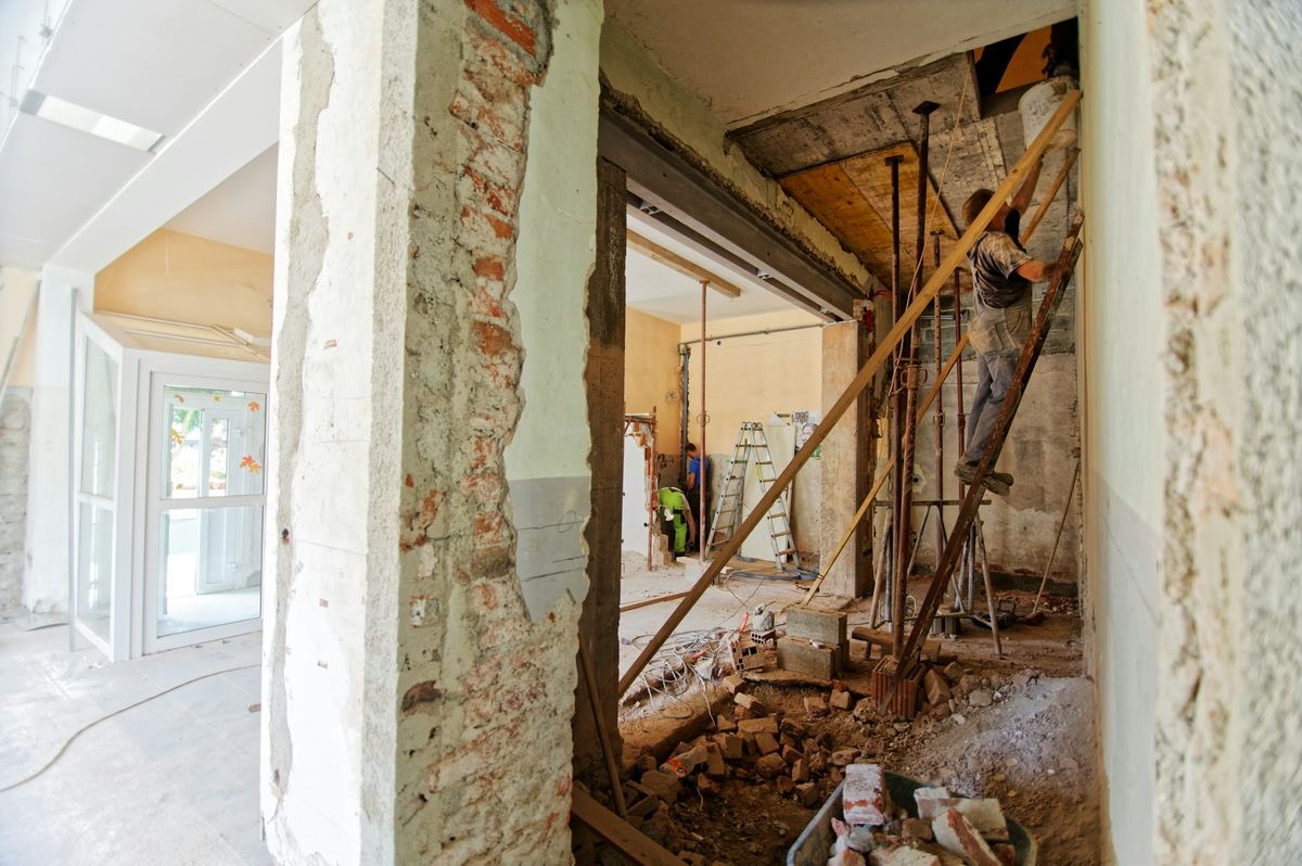 Woning tijdens de afbraak: muren opengekapt, puin op de vloer, een werkman op een ladder