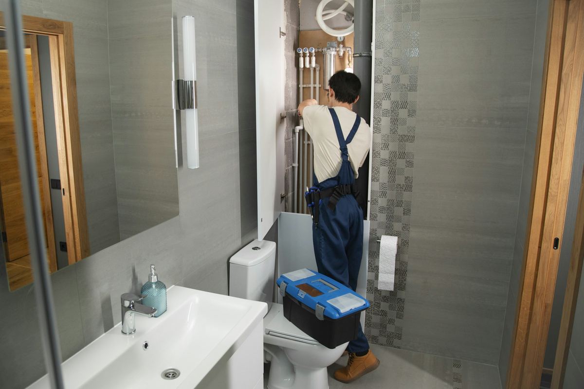 Loodgieter met gereedschapskist aan het werk in een badkamer met grijze tegels
